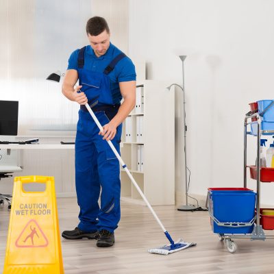 Full length of male janitor mopping floor in office
